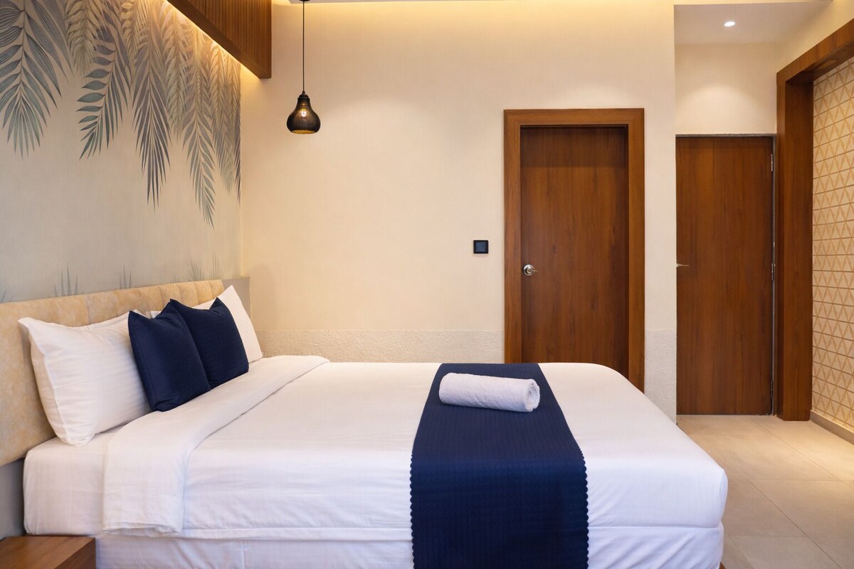 Una habitación de hotel con una cama, una mesita de noche, una lámpara de pared y una puerta.
