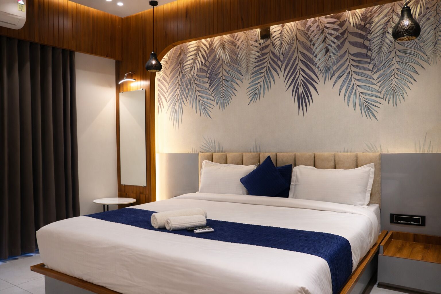 Una habitación de hotel moderna con una cama grande, una mesita de noche y una pared con un estampado de hojas.
