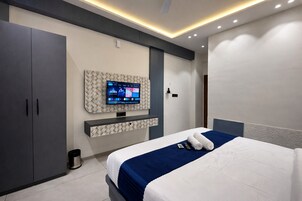 A modern hotel room with a large bed, a flat-screen TV mounted on the wall, and a wardrobe.