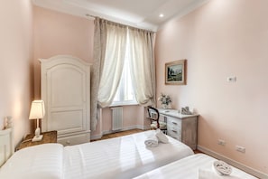 Ein Schlafzimmer mit zwei Betten, einem Schminktisch, einem Sessel, einer Lampe, einem Heizkörper und einem Bild an der Wand.