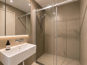 Un bagno moderno con cabina doccia in vetro, un lavandino bianco e uno specchio sopra.