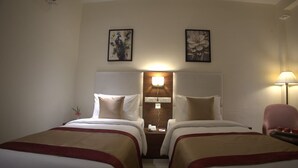 A hotel room with two beds, a nightstand with a lamp, and artwork on the walls. - Sterling Regalia Agra (Agra)