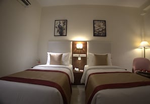 Habitación de hotel con dos camas, una mesita de noche con lámpara y cuadros en las paredes.