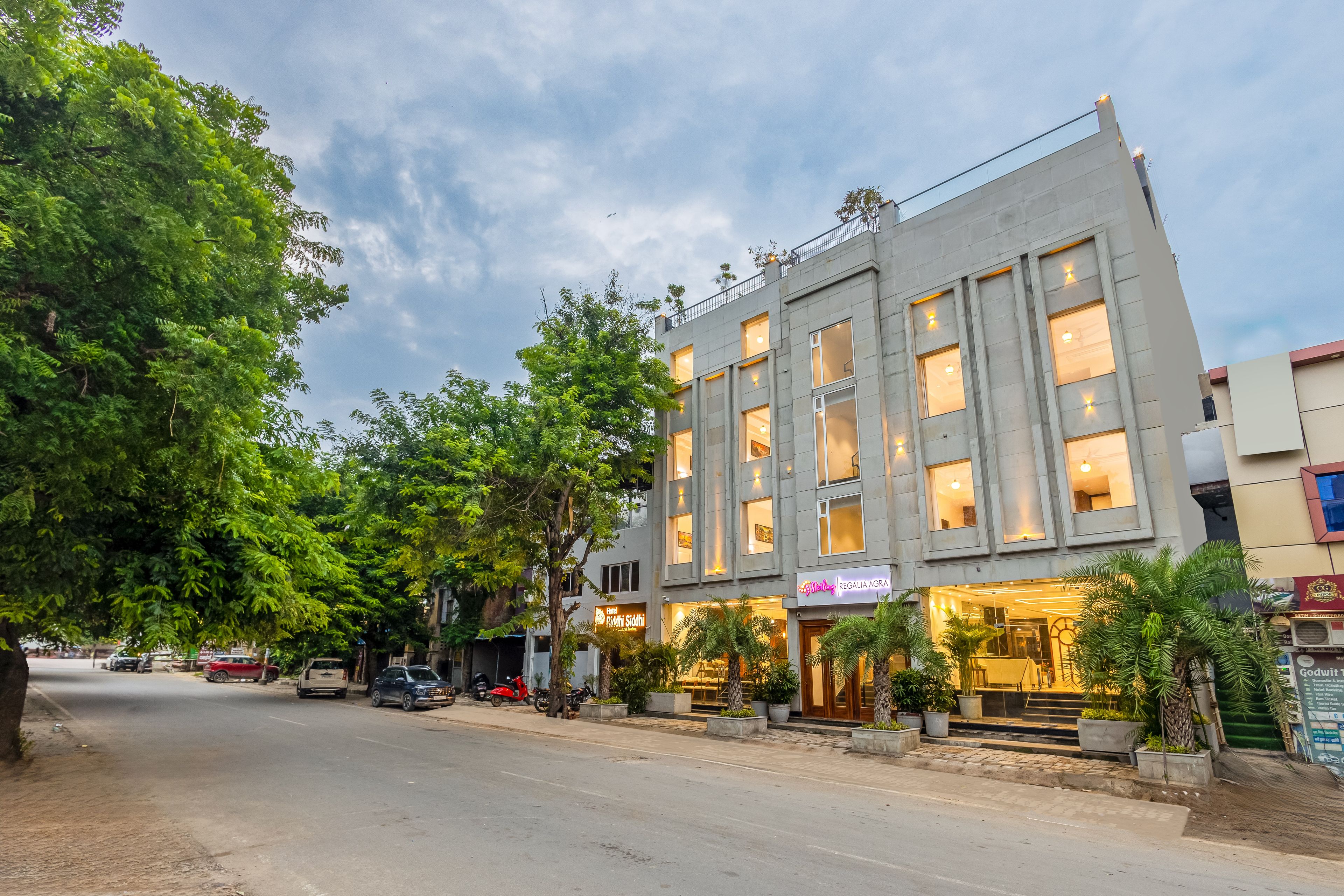 Un hotel con fachada moderna, numerosas ventanas y un área de entrada bien cuidada con plantas en macetas.