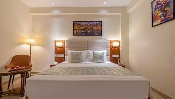 Una camera d'albergo con un letto grande, abat-jour, una sedia, un tavolino con delle mele e un quadro appeso al muro.