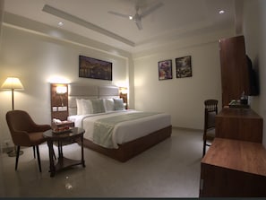 Una habitación de hotel con cama, escritorio, silla, lámpara y obras de arte en las paredes.