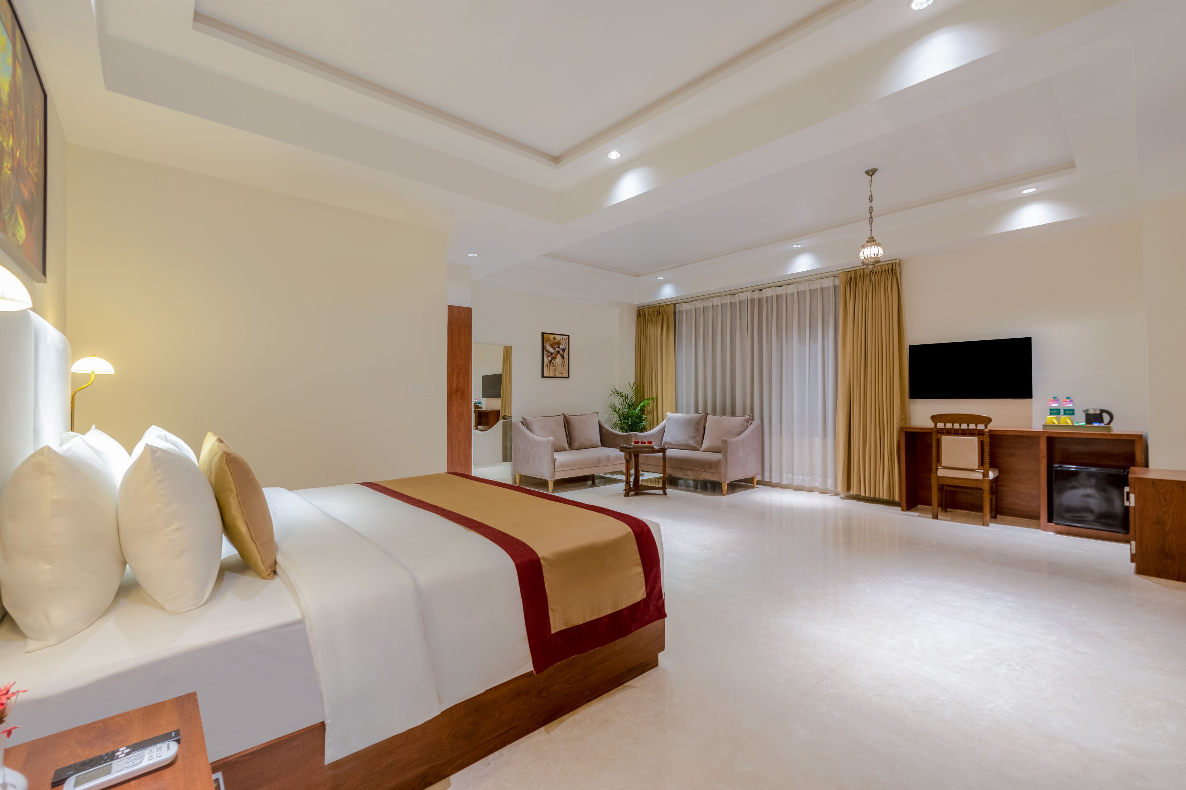 Habitación de hotel con cama, escritorio, televisor y zona de estar con sofá y sillones.