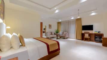 Habitación de hotel con cama, escritorio, televisor y zona de estar con sofá y sillones.
