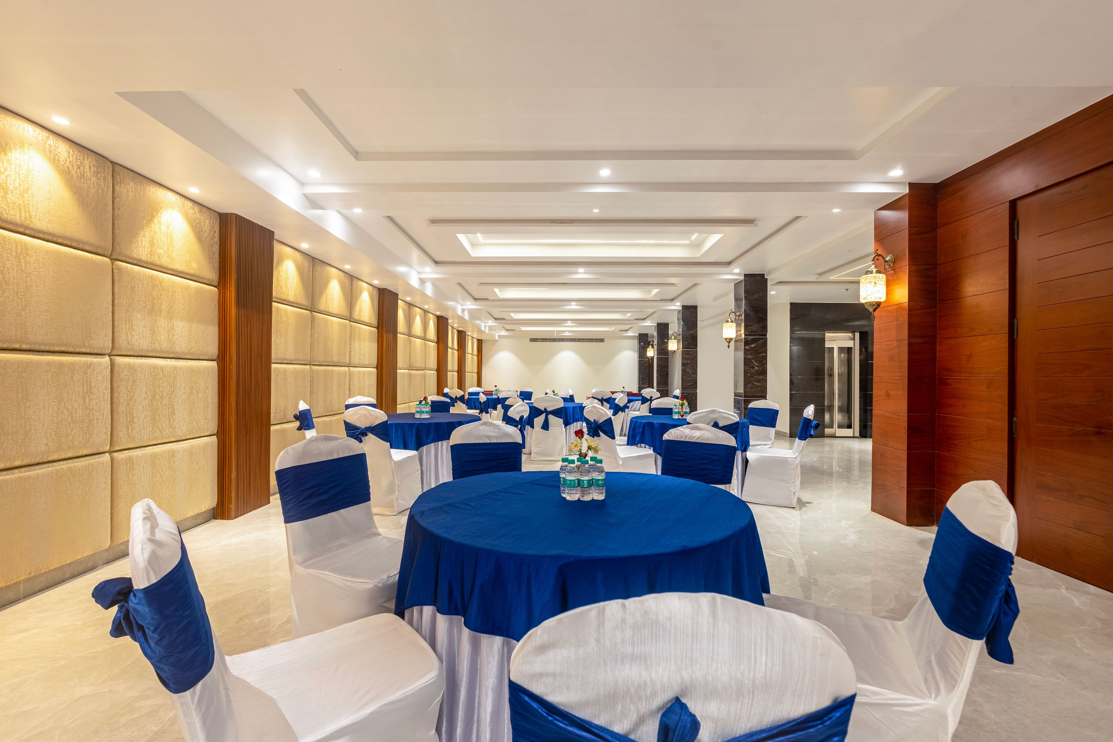 Una sala conferenze con tavoli rotondi, sedie bianche con fiocchi azzurri e un design moderno del soffitto.