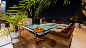 A rooftop pool area with a hot tub, lounge chairs, and potted plants.