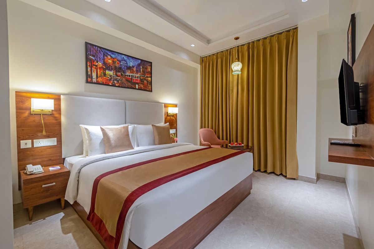 A hotel room with a large bed, a painting on the wall, a television, and a curtain.