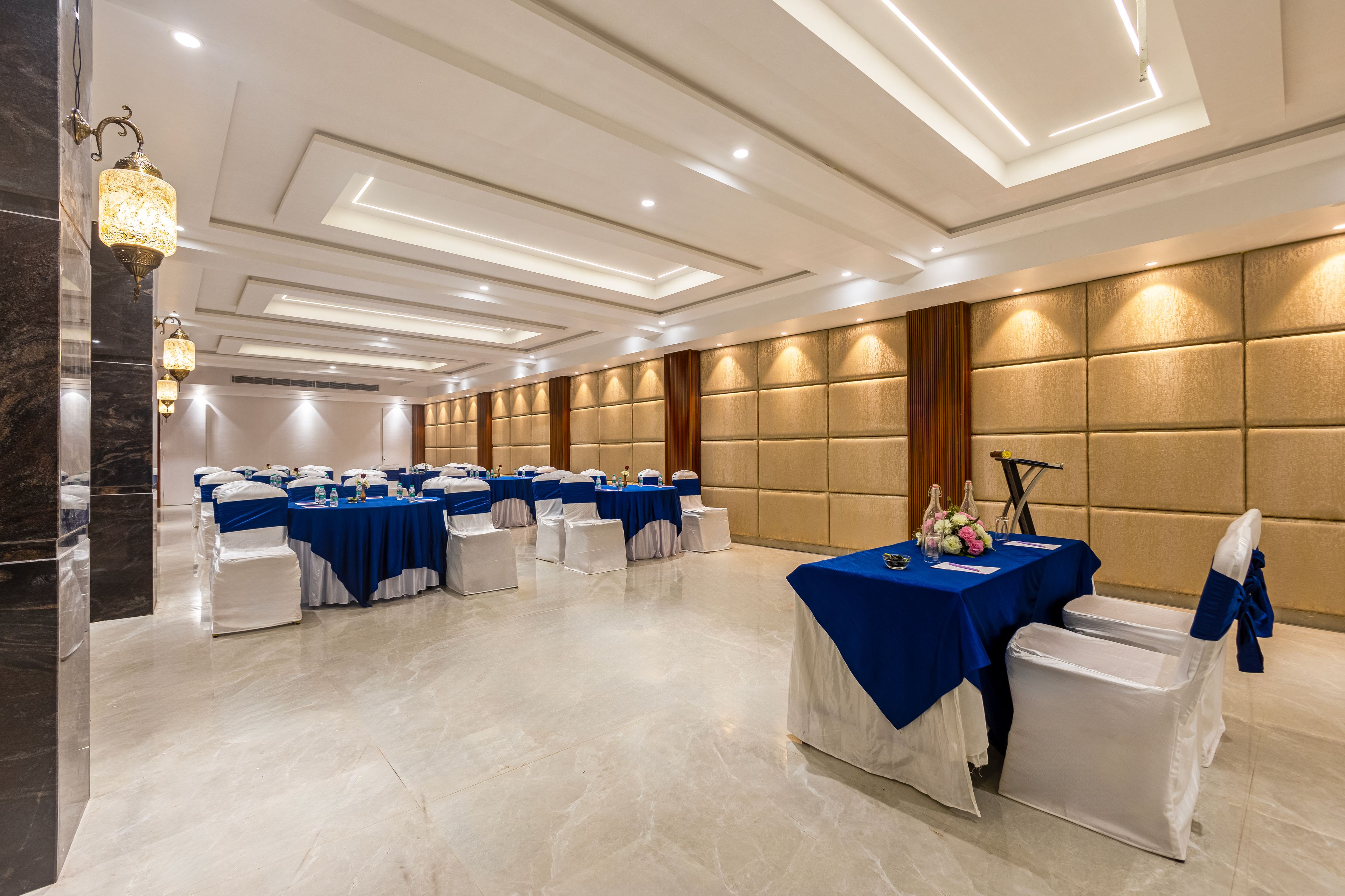 Un salón de banquetes con varias mesas, sillas blancas y piso de mármol.