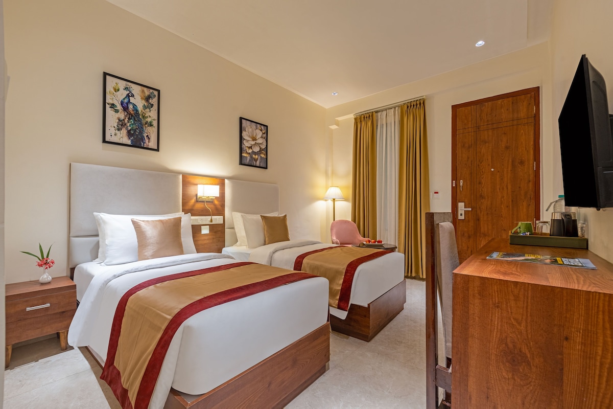 A hotel room with two beds, a desk, a television, and artwork on the walls.