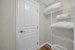 A white door with a modern handle, a white laundry basket, and white shelves with folded towels.