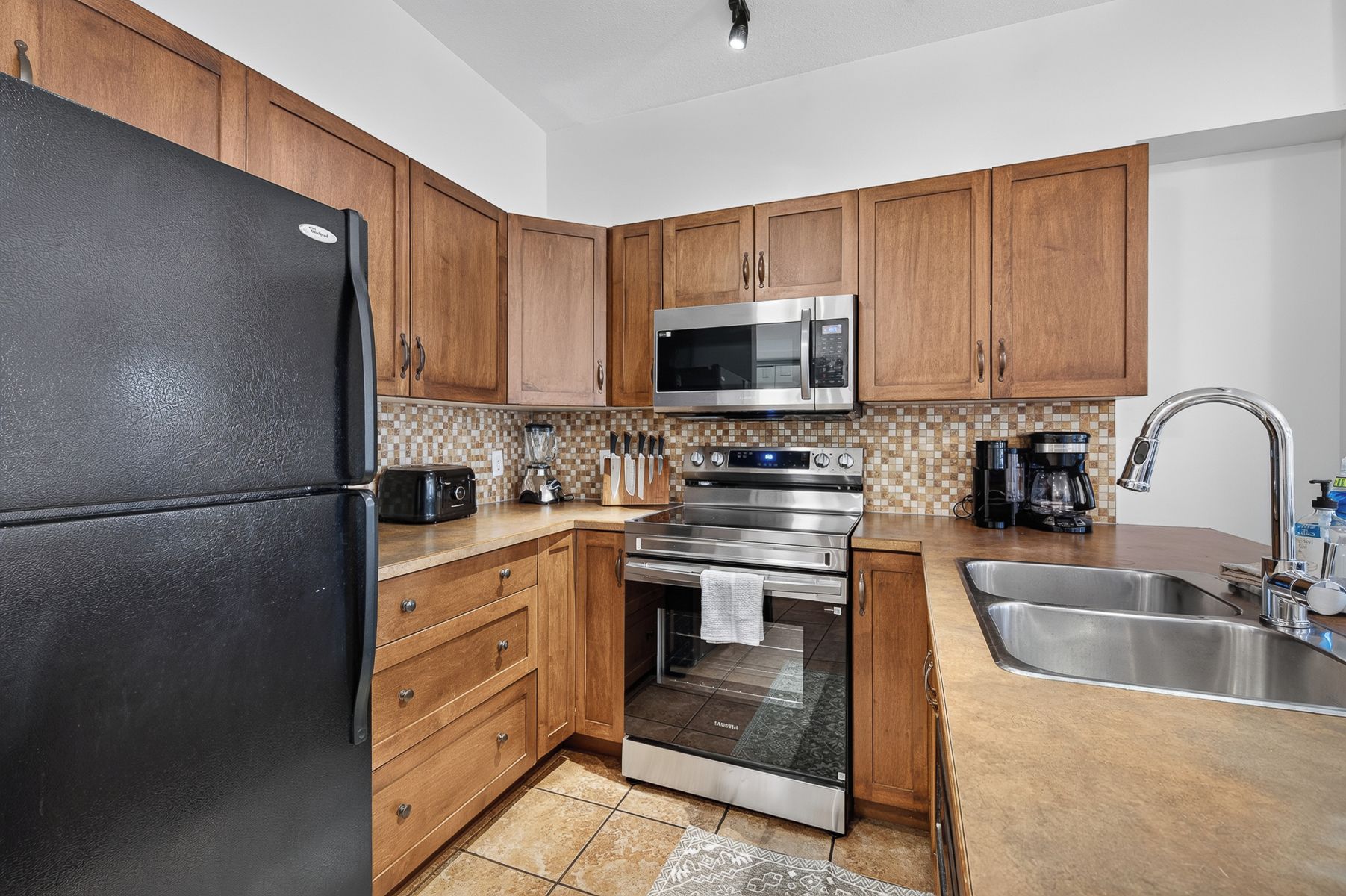 A kitchen with wooden cabinets, a stainless steel refrigerator, a microwave, an oven, and a sink.