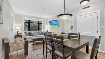 A dining area with a wooden table and chairs, a sofa, and a television mounted on the wall.