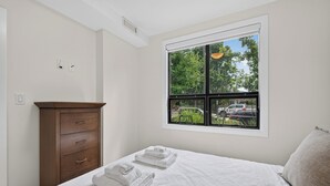 Quarto com cama, cómoda de madeira, janela com vista para o exterior e luminária no teto.