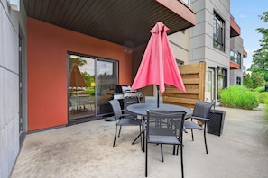 An outdoor patio with a table and chairs, a grill, and a pink umbrella.