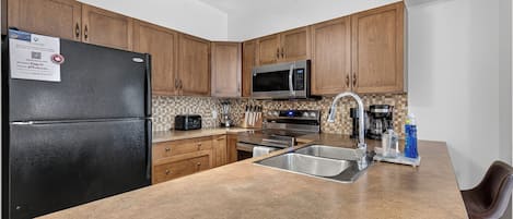 A kitchen with wooden cabinets, a black refrigerator, a microwave, a stove, and a sink.