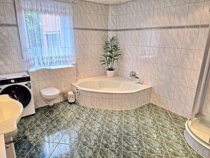 Ein Badezimmer mit Waschmaschine, Toilette, Badewanne und einer Zimmerpflanze.