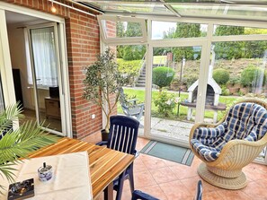 Ein Wintergarten mit einem Holztisch, Korbstühlen und einer Topfpflanze.