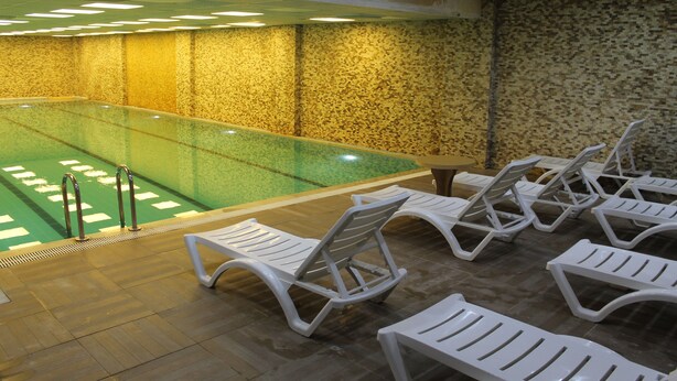 An indoor swimming pool with a tiled floor, a pool ladder, and white lounge chairs arranged around the pool. - GRAND ALİN HOTEL (Turhal)
