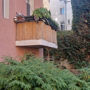 Ein Balkon mit Bambuszaun, einer Topfpflanze und Blick auf ein mit Efeu bewachsenes Gebäude.
