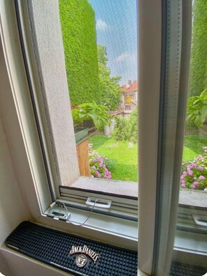 Ein Fenster mit Blick auf einen gepflegten Garten, einen Holzzaun und ein Haus im Hintergrund.