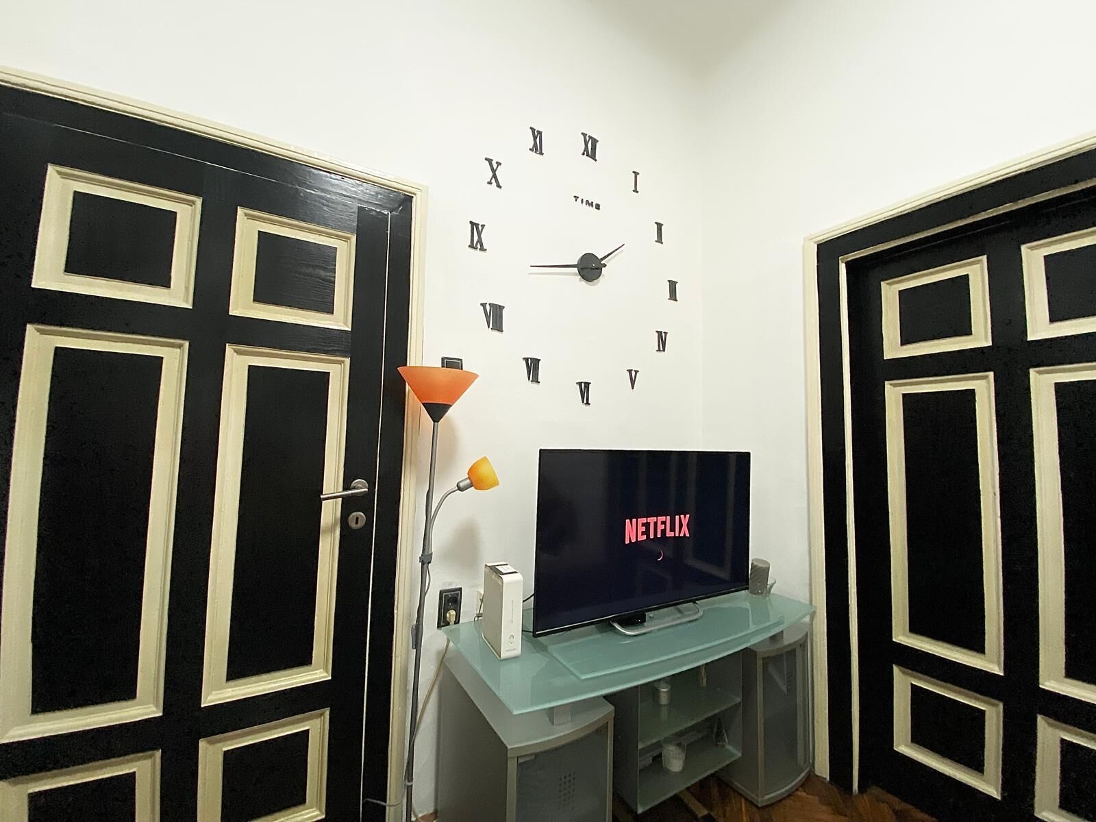 A room with a wall clock, a television, and a door with a decorative frame.