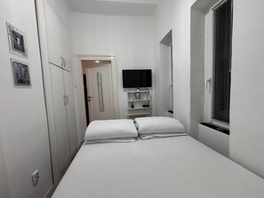 Un dormitorio con cama, armario, televisor y ventana con persianas.