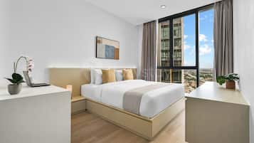 A modern hotel room with a large bed, a desk, and a view of the cityscape.