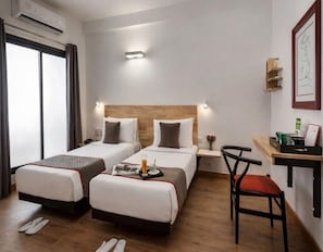 A hotel room with two beds, a desk, a chair, and a window.