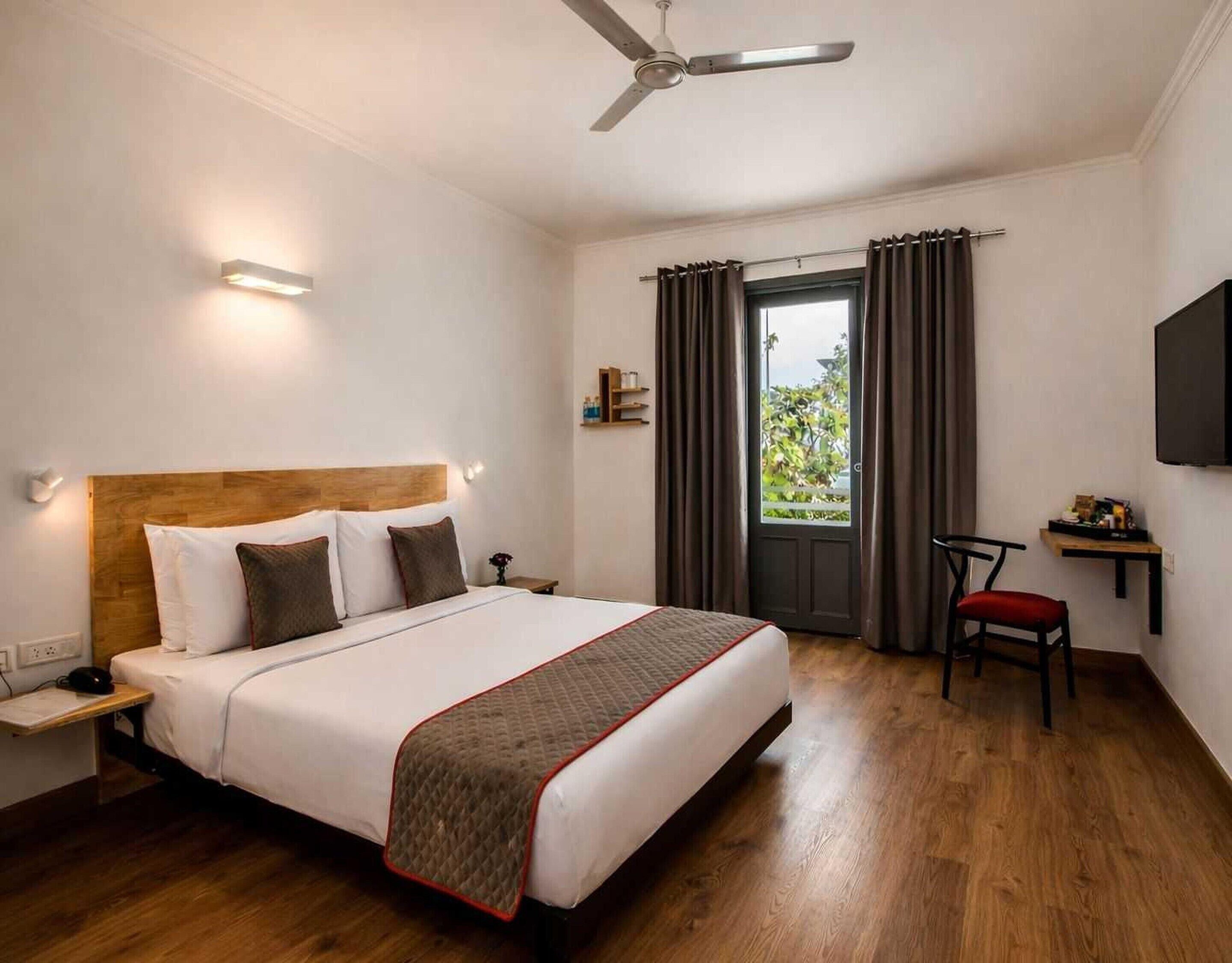 Une chambre d’hôtel avec un lit, une table de chevet, une chaise et un téléviseur fixé au mur.