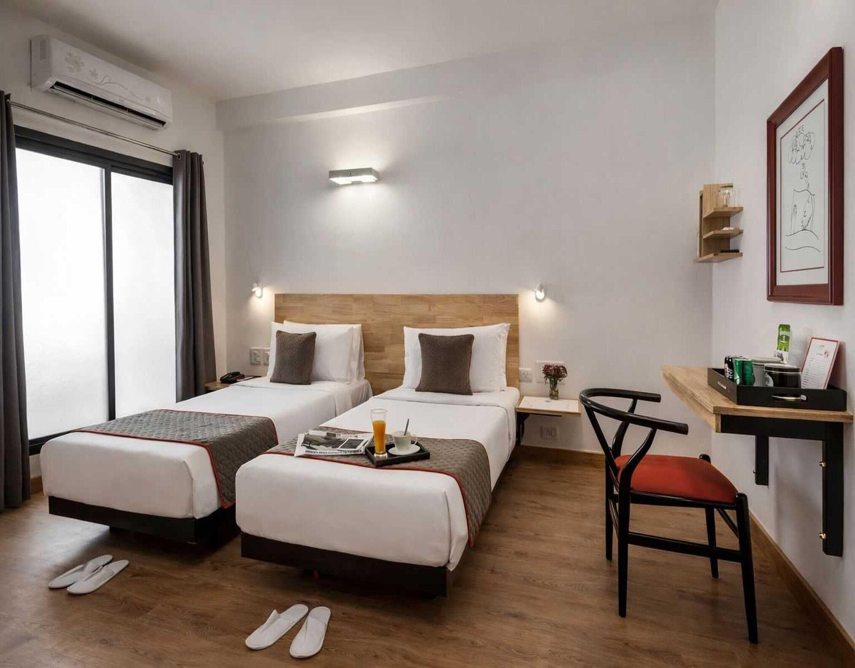 A hotel room with two beds, a desk, a chair, and a small table.