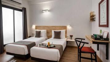A hotel room with two beds, a desk, a chair, and a small table.