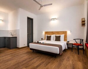 Una habitación de hotel con cama, mesita de noche, silla, armario y ventilador de techo.