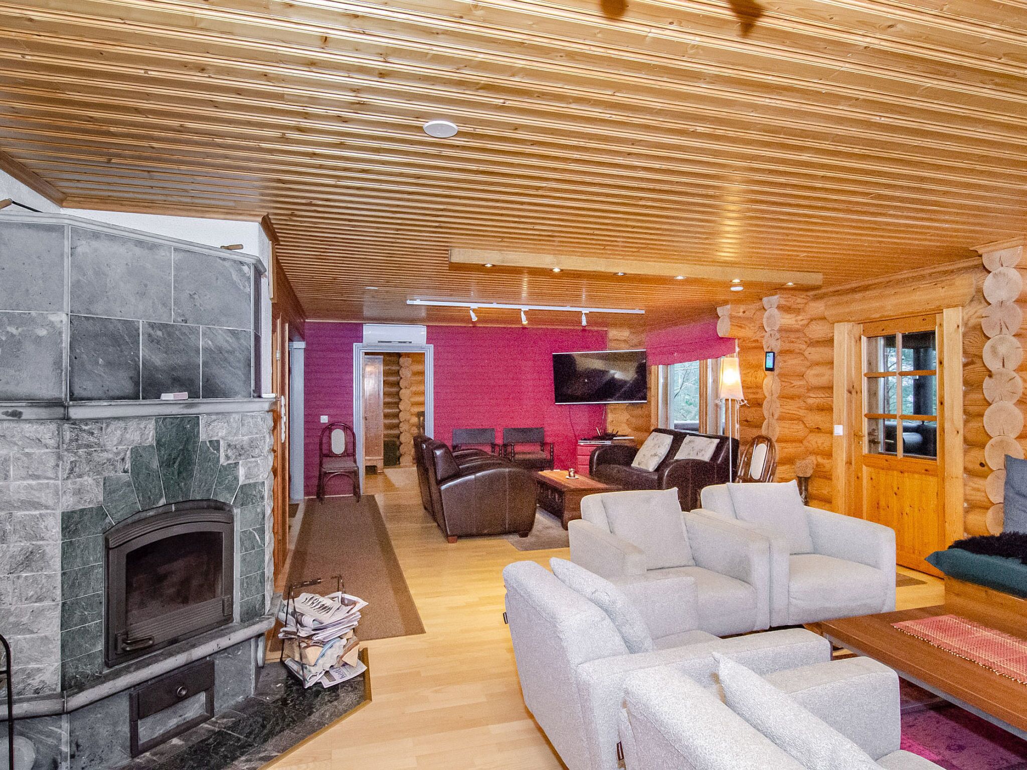 Een houten blokhut interieur met een stenen open haard, een aan de muur bevestigde televisie en een zithoek met banken en stoelen.