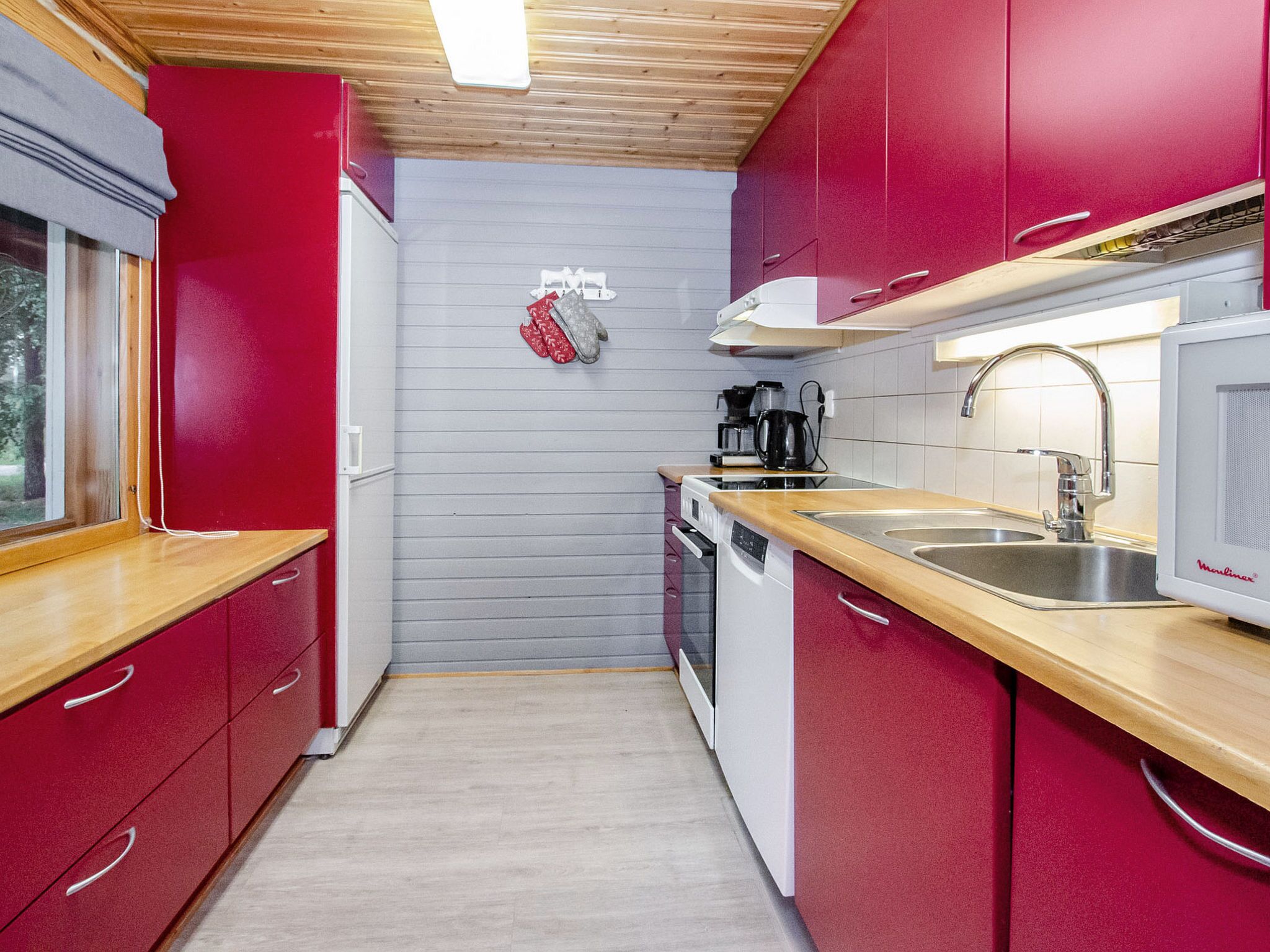 Een kleine keuken met rode kastjes, een roestvrijstalen spoelbak en een magnetron.