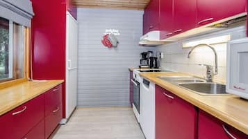 Een kleine keuken met rode kastjes, een roestvrijstalen spoelbak en een magnetron.