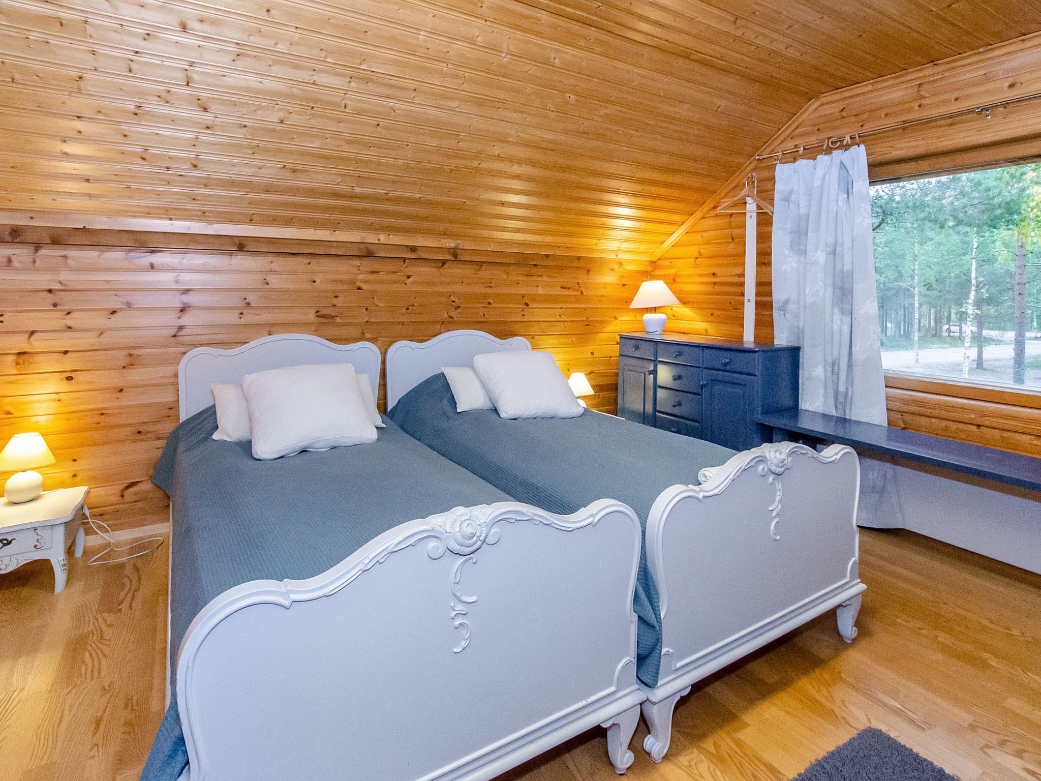 Une chambre dans un chalet en bois, avec un lit double, des lampes de chevet et une fenêtre donnant sur la forêt.