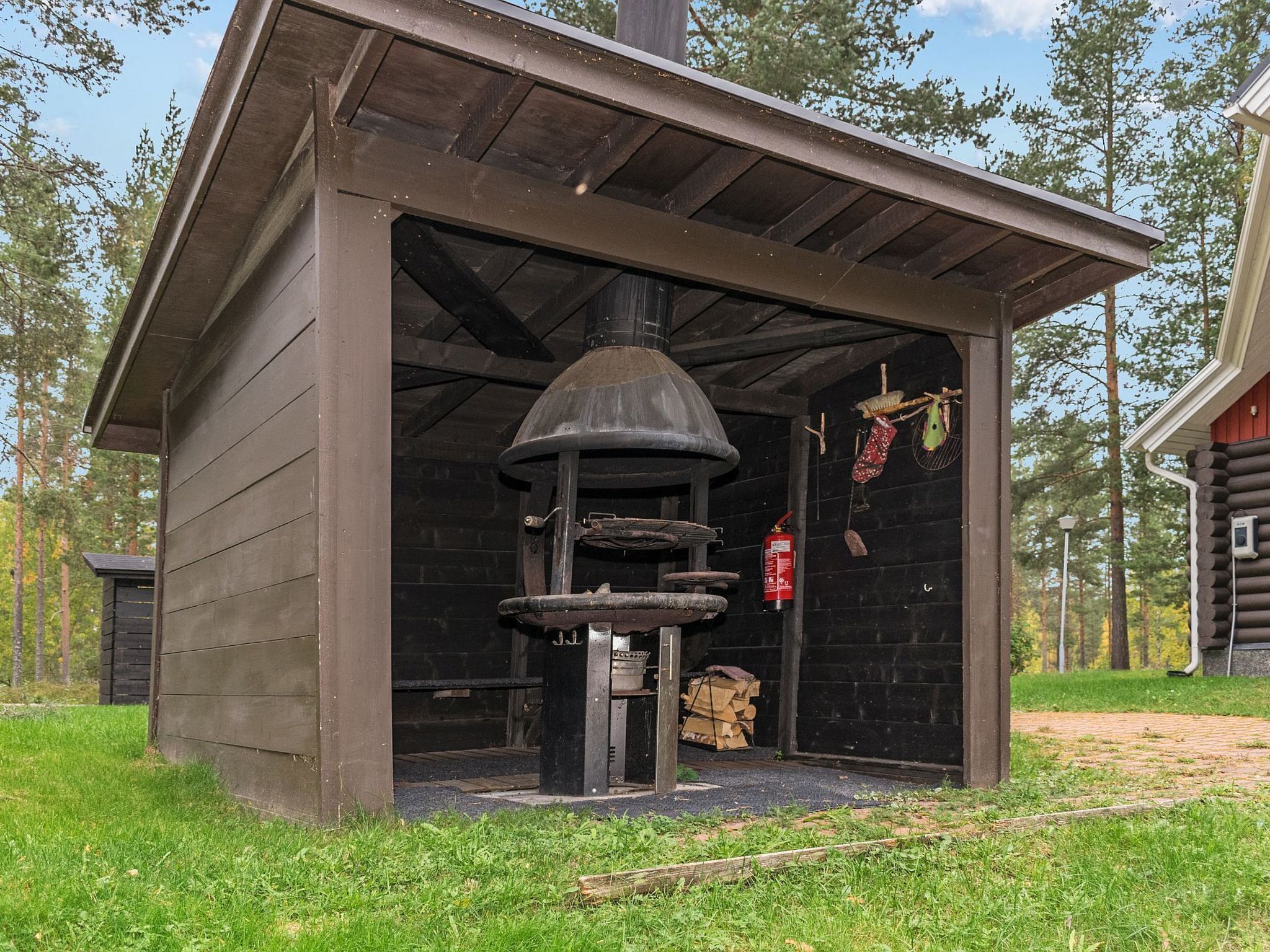 A rustic outdoor cooking area with a chimney, a fire extinguisher, and a stack of firewood.