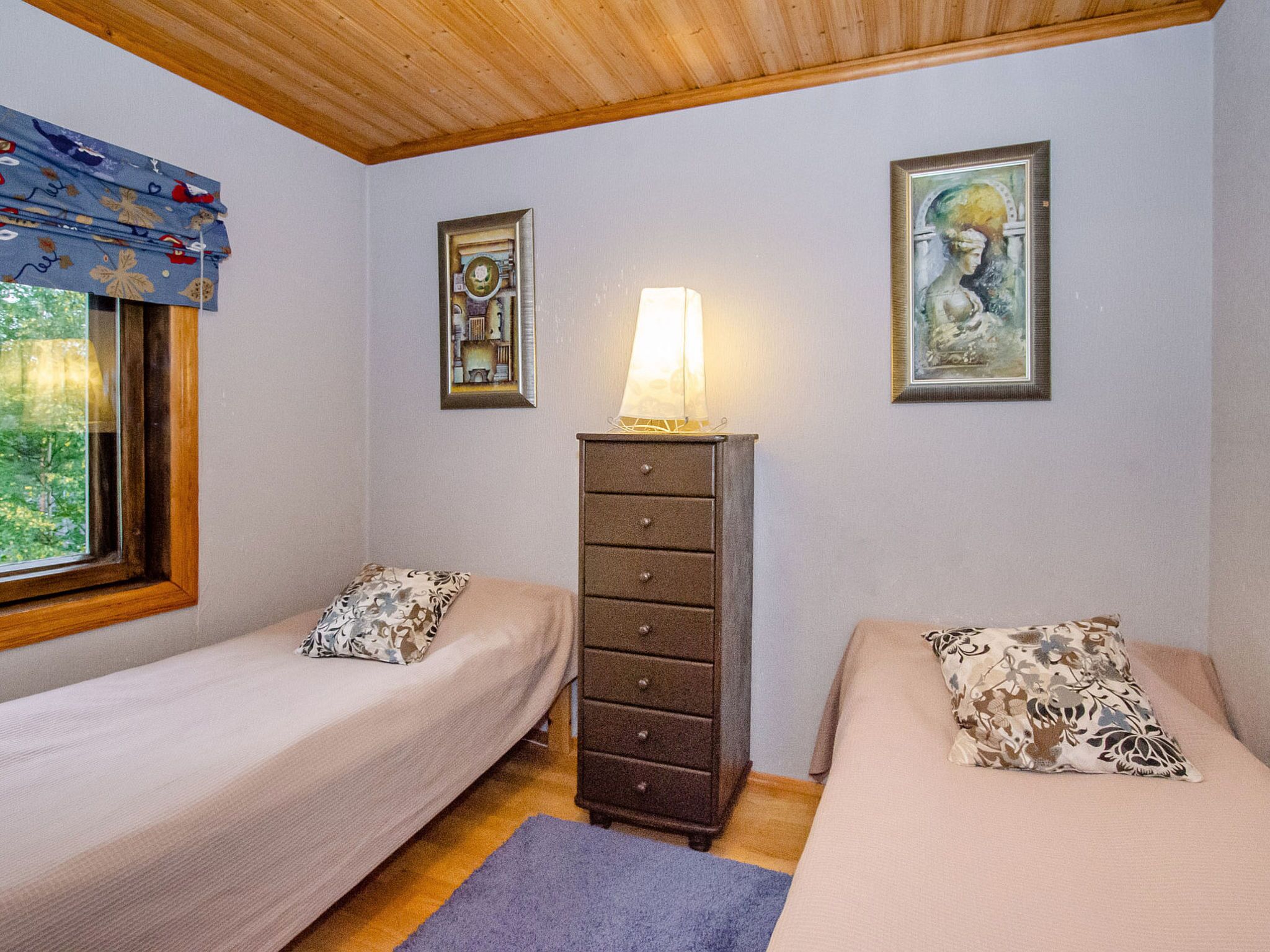 A room with two beds, a dresser, a lamp, and two framed pictures on the wall.