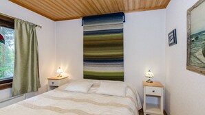 Quarto com cama, duas mesas de cabeceira com luminárias, janela com cortinas, tapeçaria de parede e um quadro emoldurado.