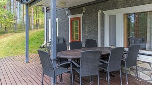 Um terraço ao ar livre com uma mesa redonda e seis cadeiras, uma parede de pedra e uma porta com moldura vermelha.