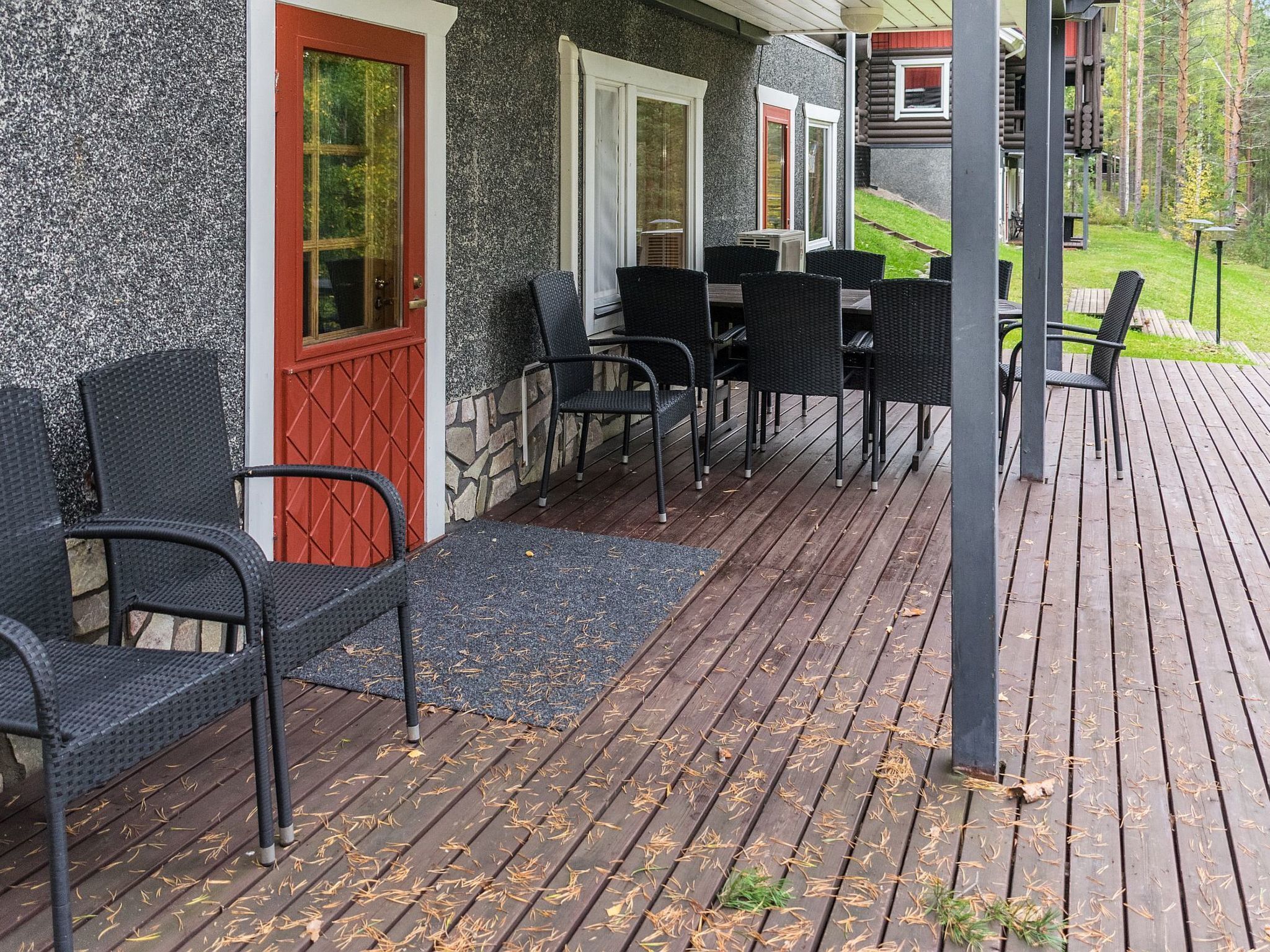 A covered outdoor seating area with chairs and a table, a red door, and a stone wall.