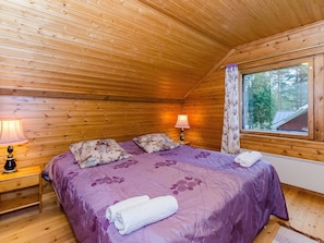 Een knus slaapkamer in een houten hutje, met een bed, twee bedlampen en een raam met uitzicht op bomen.
