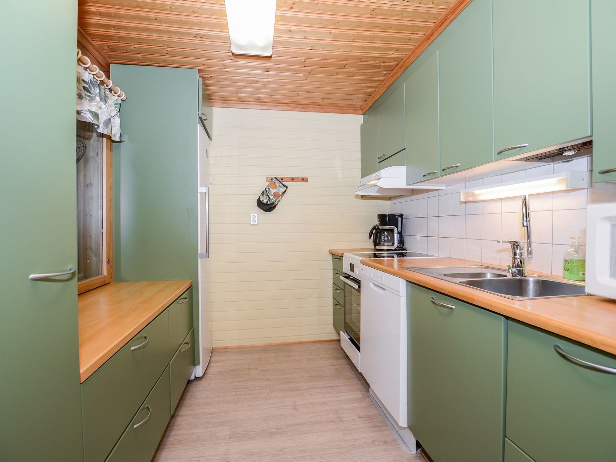 Een kleine keuken met houten kastjes, een inbouwoven en een spoelbak.
