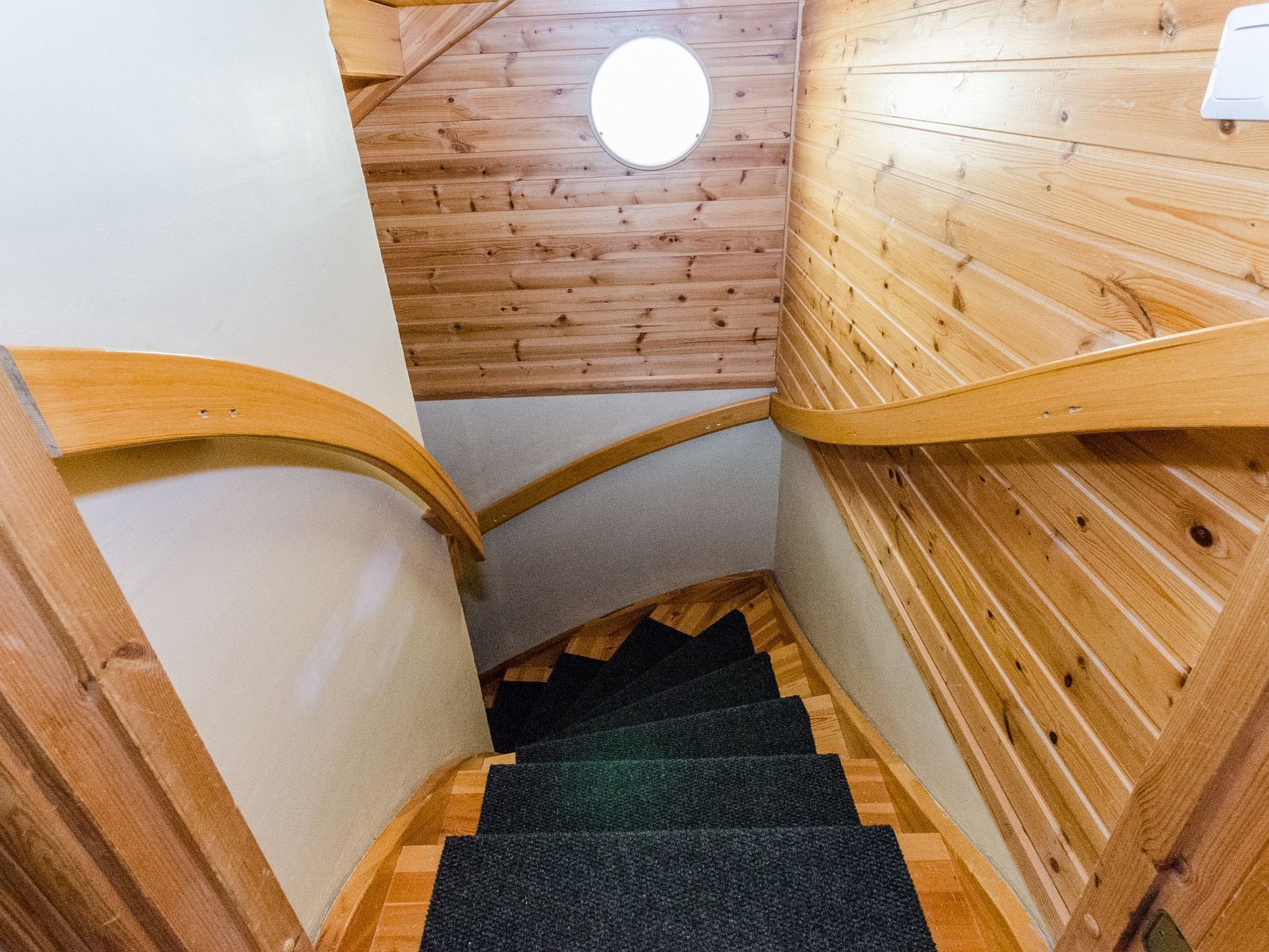 Een houten trap met beklede treden die leidt naar een kamer met een houten plafond en een ronde lamp.