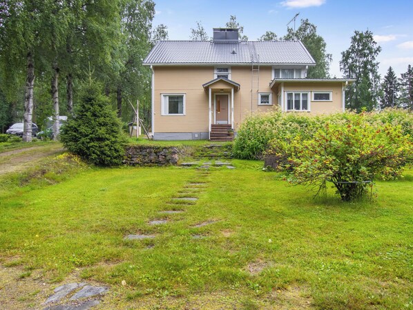 A two-story house with a front porch, a stone pathway leading to the entrance, and a well-maintained lawn. - Vacation home Alpola by Interhome (Suomussalmi)