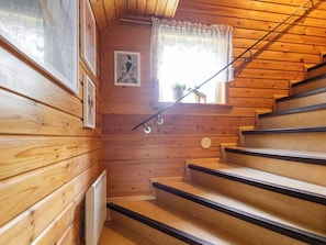 A wooden staircase with a handrail, a window with lace curtains, and framed pictures on the wall.